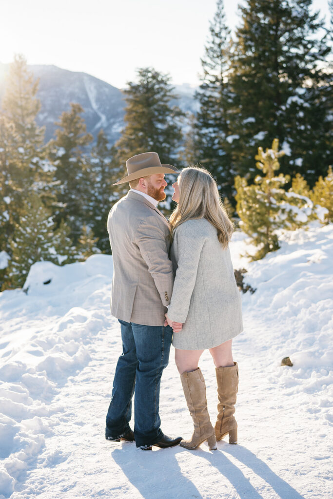 Romantic Vail, Colorado winter engagement session shows couple on bridge surrounded by snow and trees.