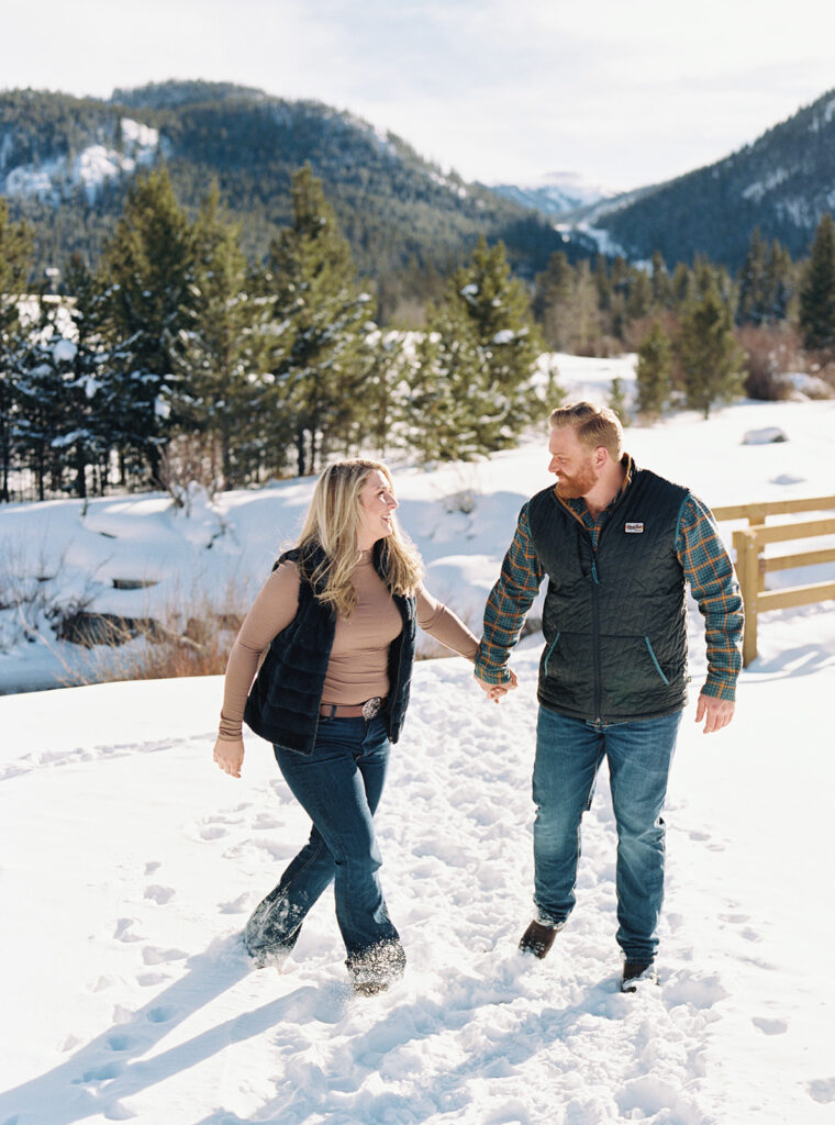 Couple stands in the snow with mountain backdrop in winter engagement session in Vail, Colorado.