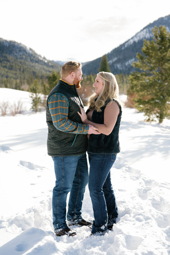 Couple stands in the snow with mountain backdrop in winter engagement session in Vail, Colorado.