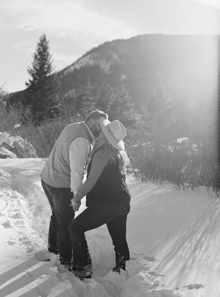 Romantic Vail, Colorado winter engagement session shows couple cuddling in snow with mountain view.