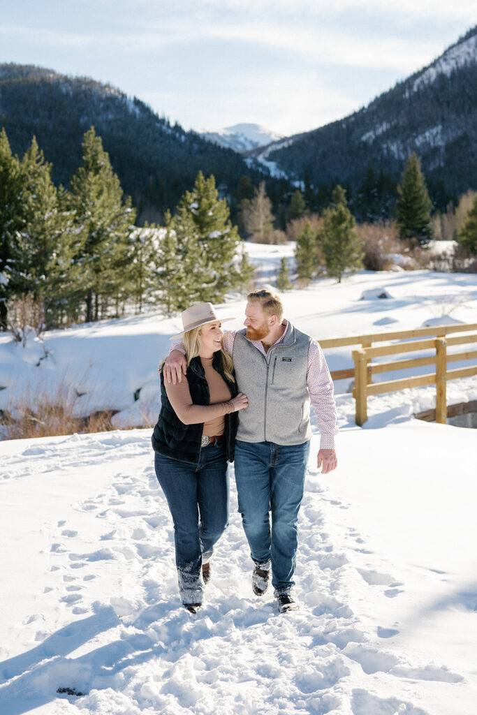 Cozy winter engagement session in Vail, Colorado captures couple smiling with stunning mountain view.