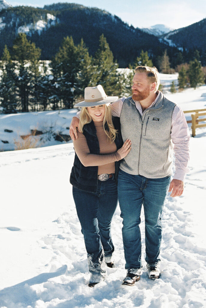 Romantic Vail, Colorado winter engagement session shows couple on bridge surrounded by snow and trees.