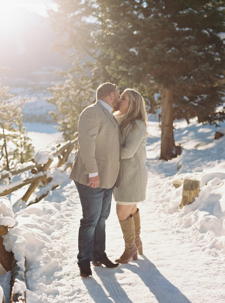 Romantic Vail, Colorado winter engagement session shows couple cuddling in snow with mountain view.