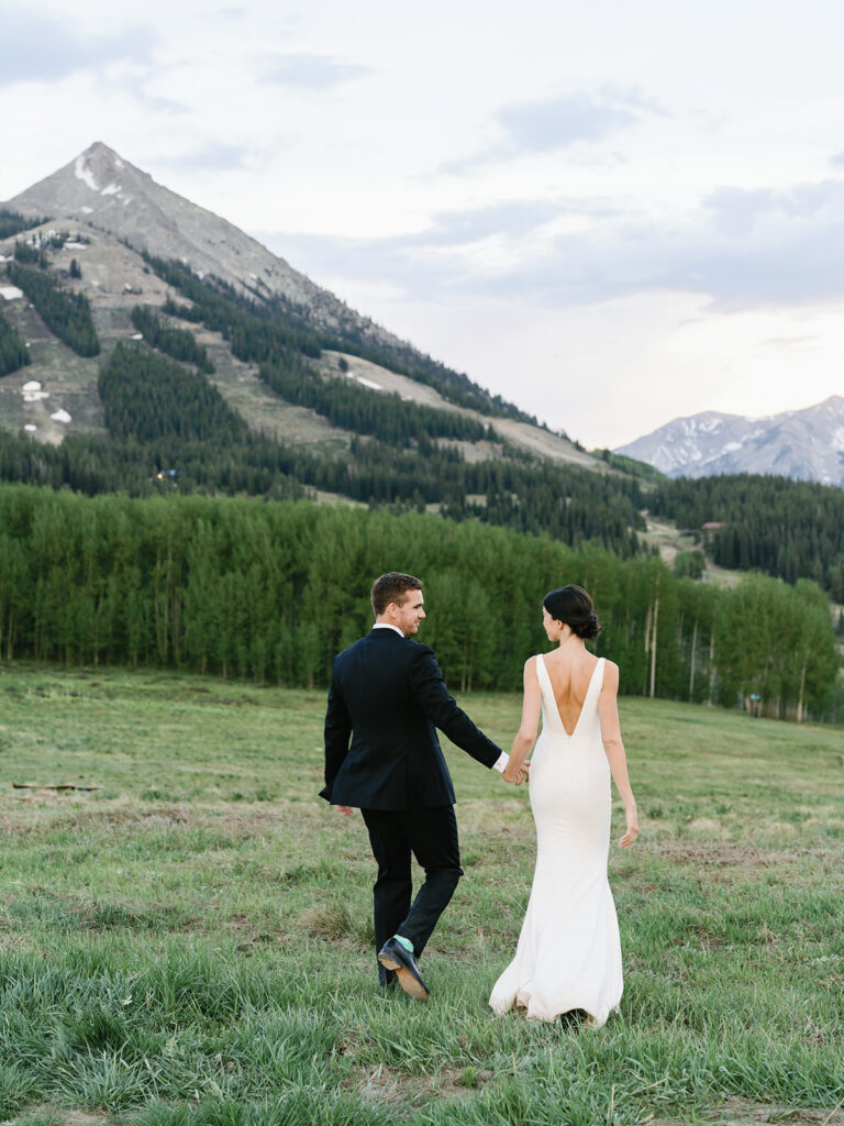 A couple embracing in a field of colorful wildflowers, with mountains towering behind them.