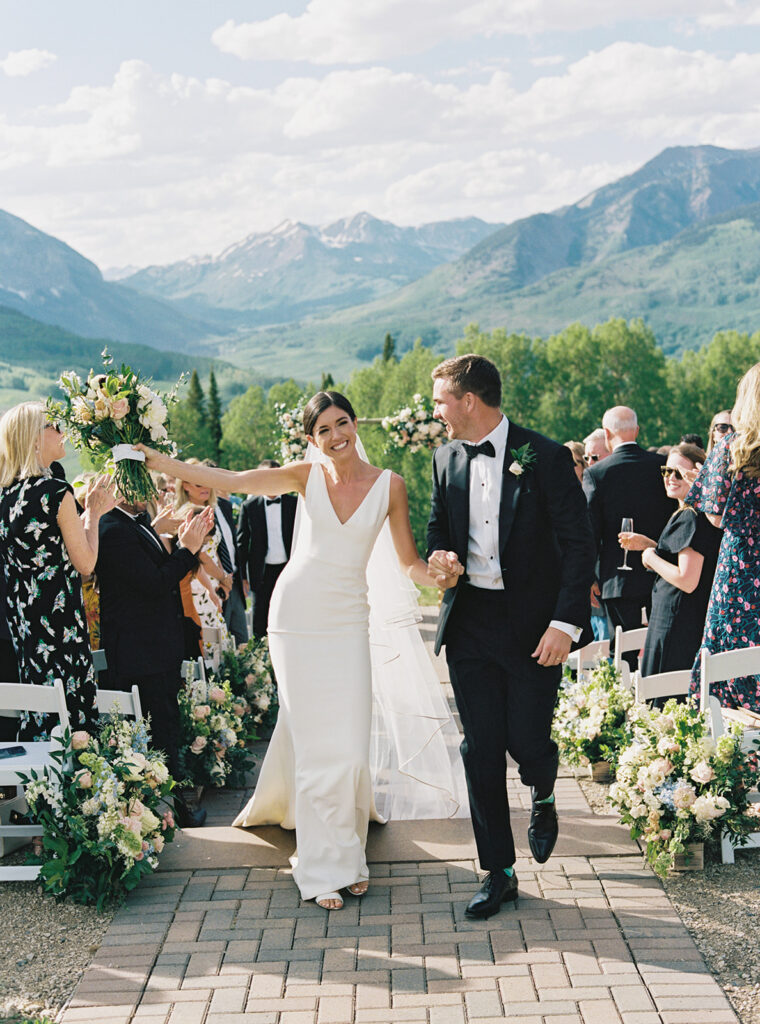A view of a wedding ceremony in progress, with guests seated in white chairs and a mountain range in the background.