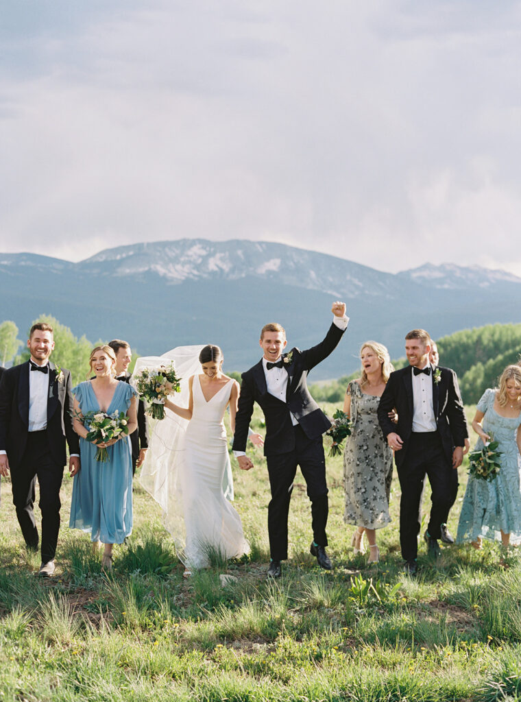 A group photo of the wedding party, with the mountains and blue sky in the background.