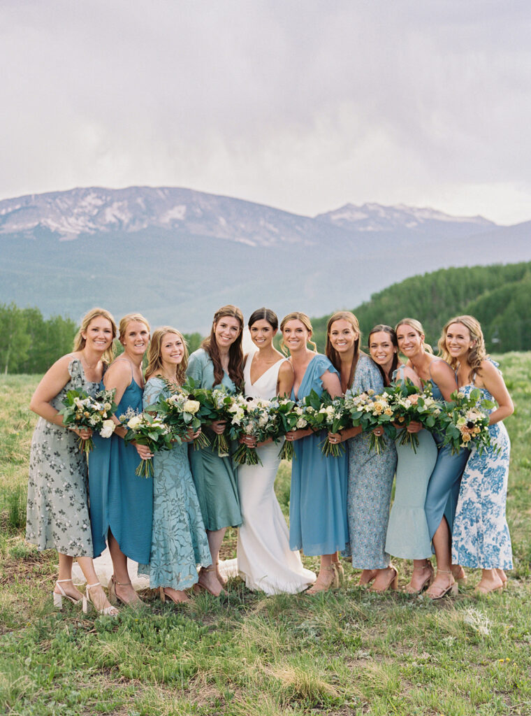 A group photo of the wedding party, with the mountains and blue sky in the background.