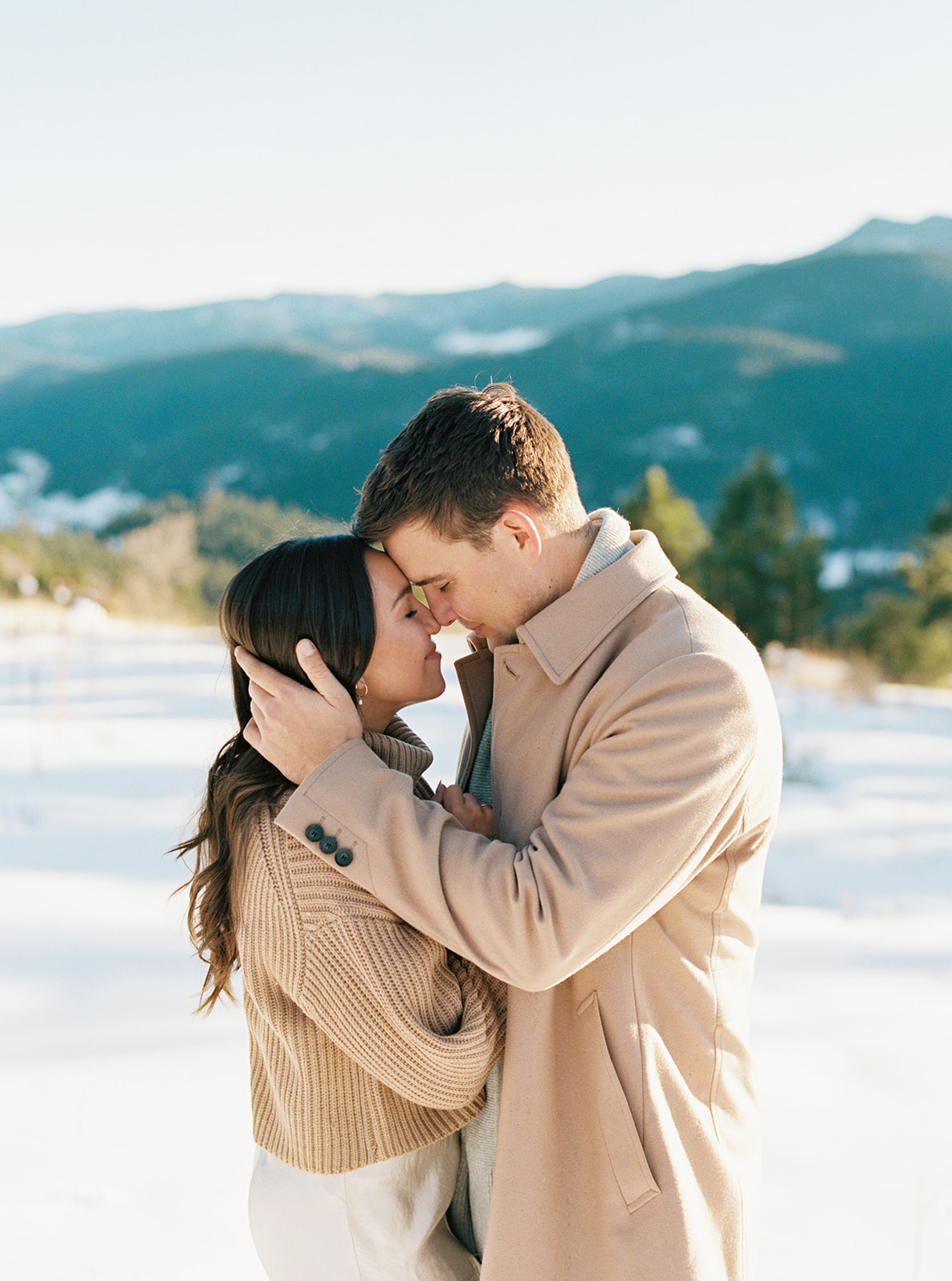 An engagement photo of a couple in love, standing in a winter wonderland with the breathtaking Front Range Mountains in the distance.
