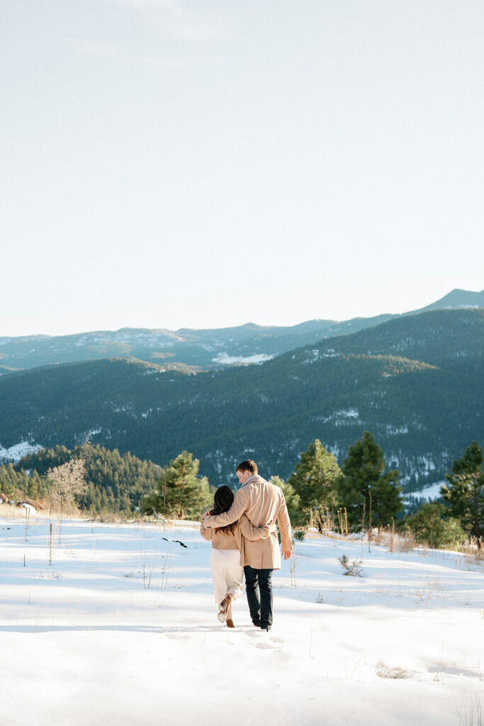 An engagement photo of a couple in love, standing in a winter wonderland with the breathtaking Front Range Mountains in the distance.