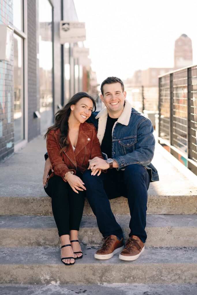 A lovely engagement photo of a couple standing in front of a towering skyscraper in downtown Denver, with the snow-covered mountains providing a stunning backdrop to their love.