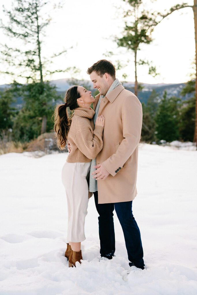 A romantic photo of a couple cuddling up to each other on a chilly winter day, with the stunning view of the Front Range mountains in the background.