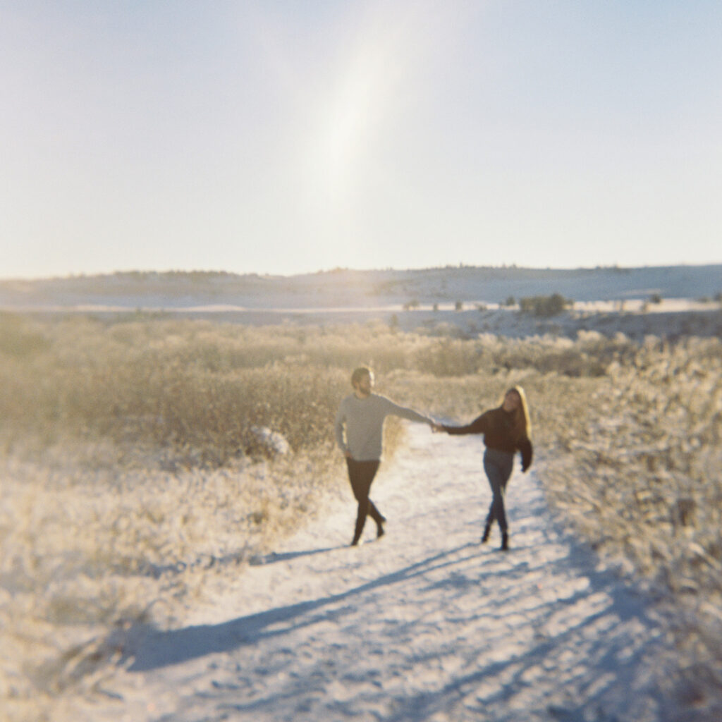 An engagement session photo of a couple in love standing close to each other, surrounded by the winter landscape, enjoying the beautiful sunrise in Boulder, Colorado.