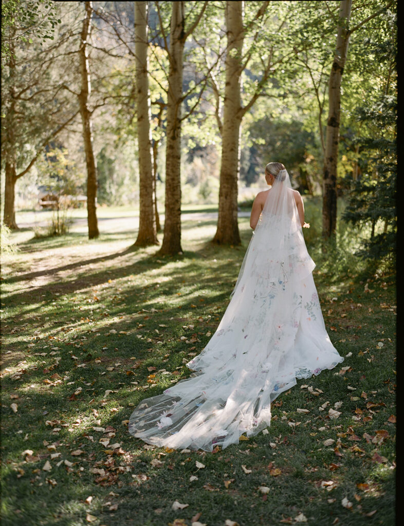 bride walking through trees with veil at Montana ranch wedding