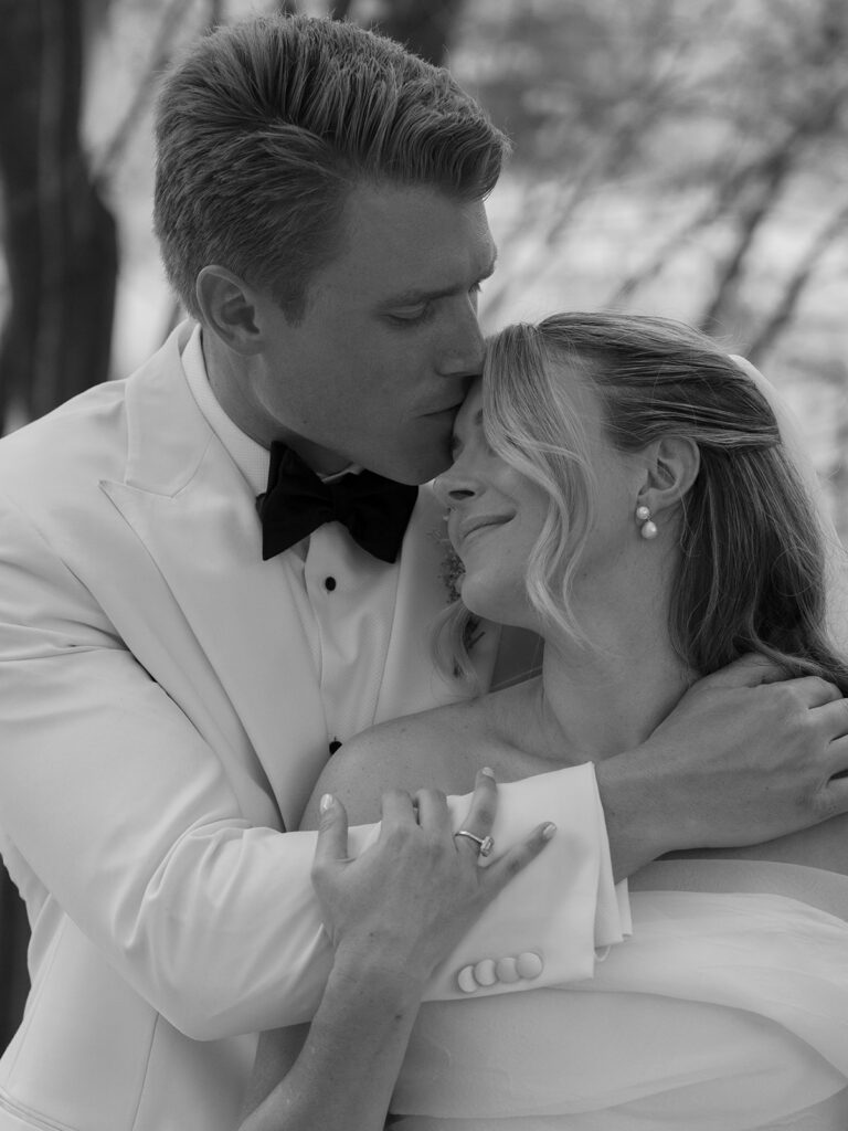 black and white portrait groom kissing bride on forehead