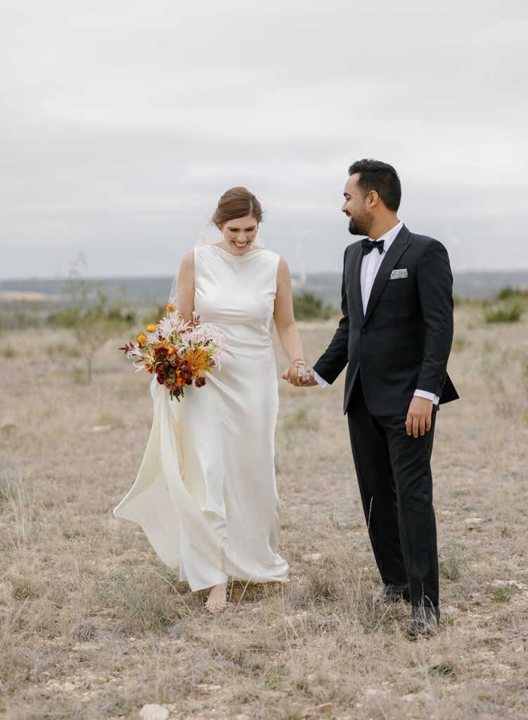 bride and groom walking through open field at ranch wedding