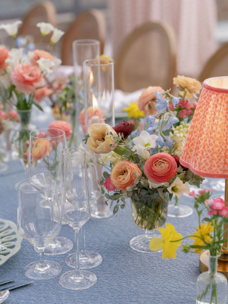 Close-up of reception table with colorful florals, candles, and glassware on textured blue linen