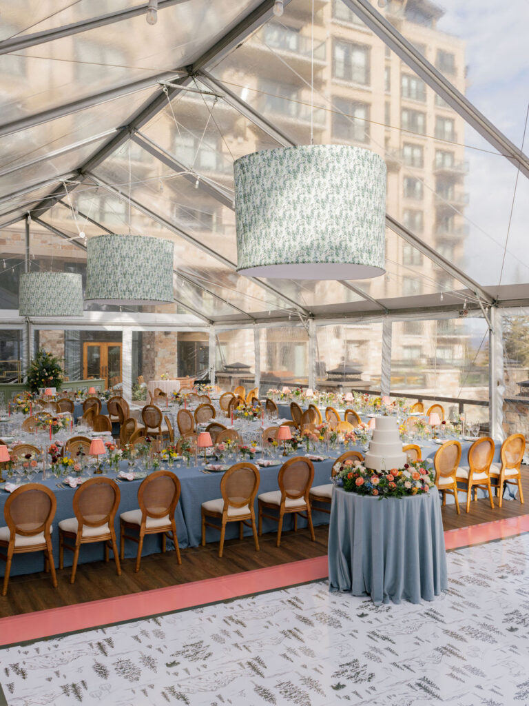 Clear-top wedding tent with long tables, blue linens, floral arrangements, and mountain views in Park City