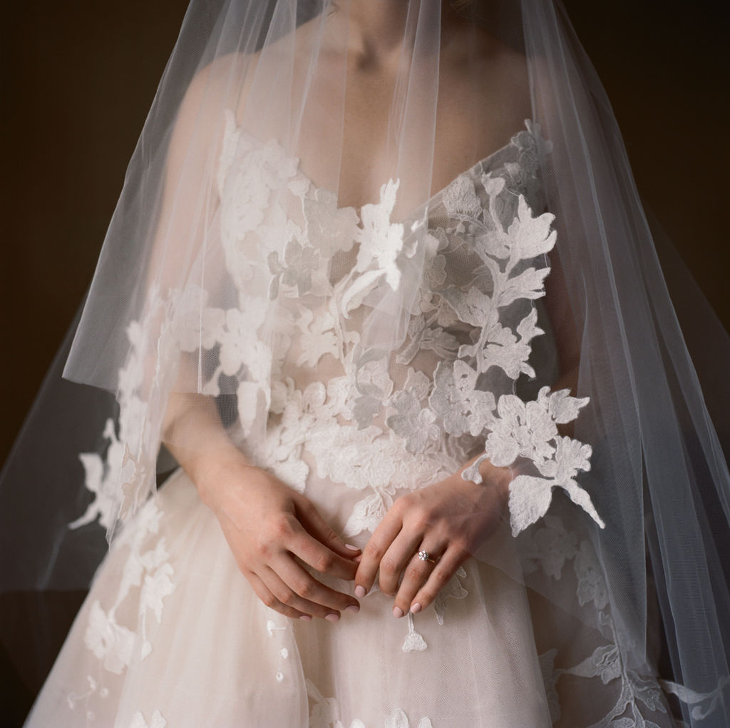 Close-up of bride’s lace wedding dress and veil highlighting texture and delicate floral appliqué